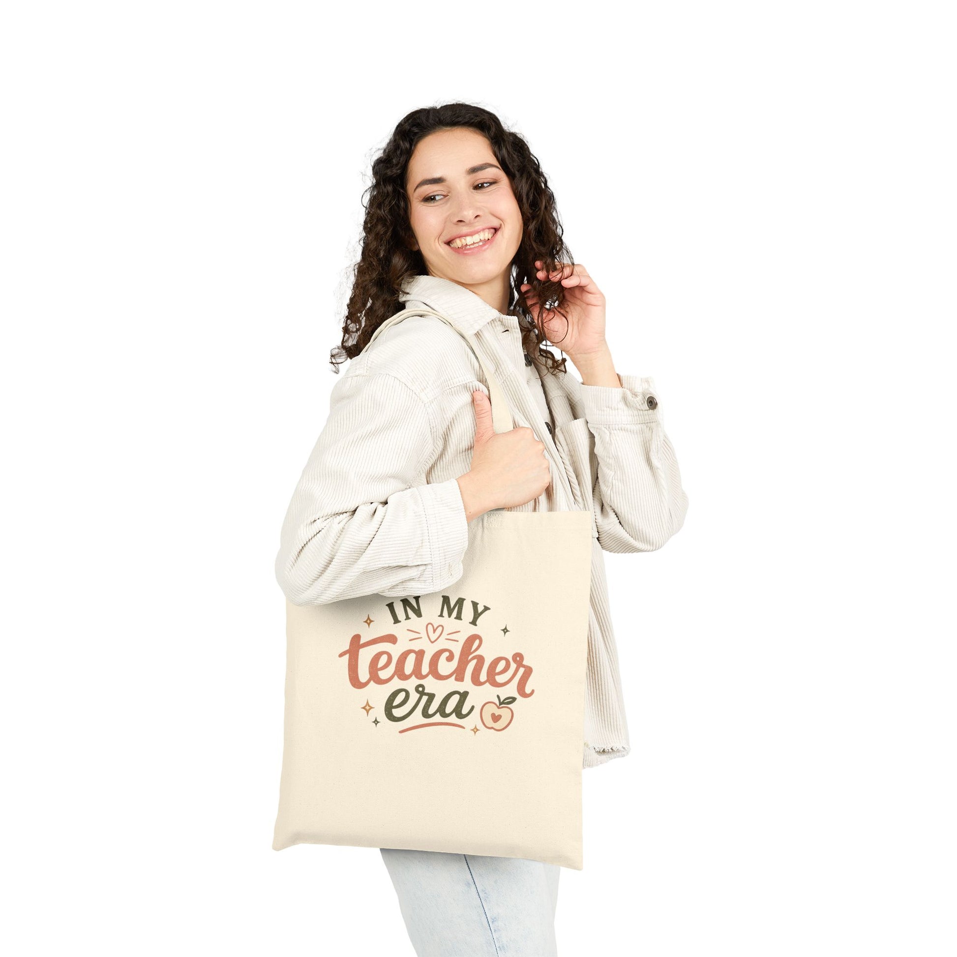 Woman holding a natural canvas tote bag with illustrations and text  that says, In My Teacher Era. It's used for the classroom or everyday use.