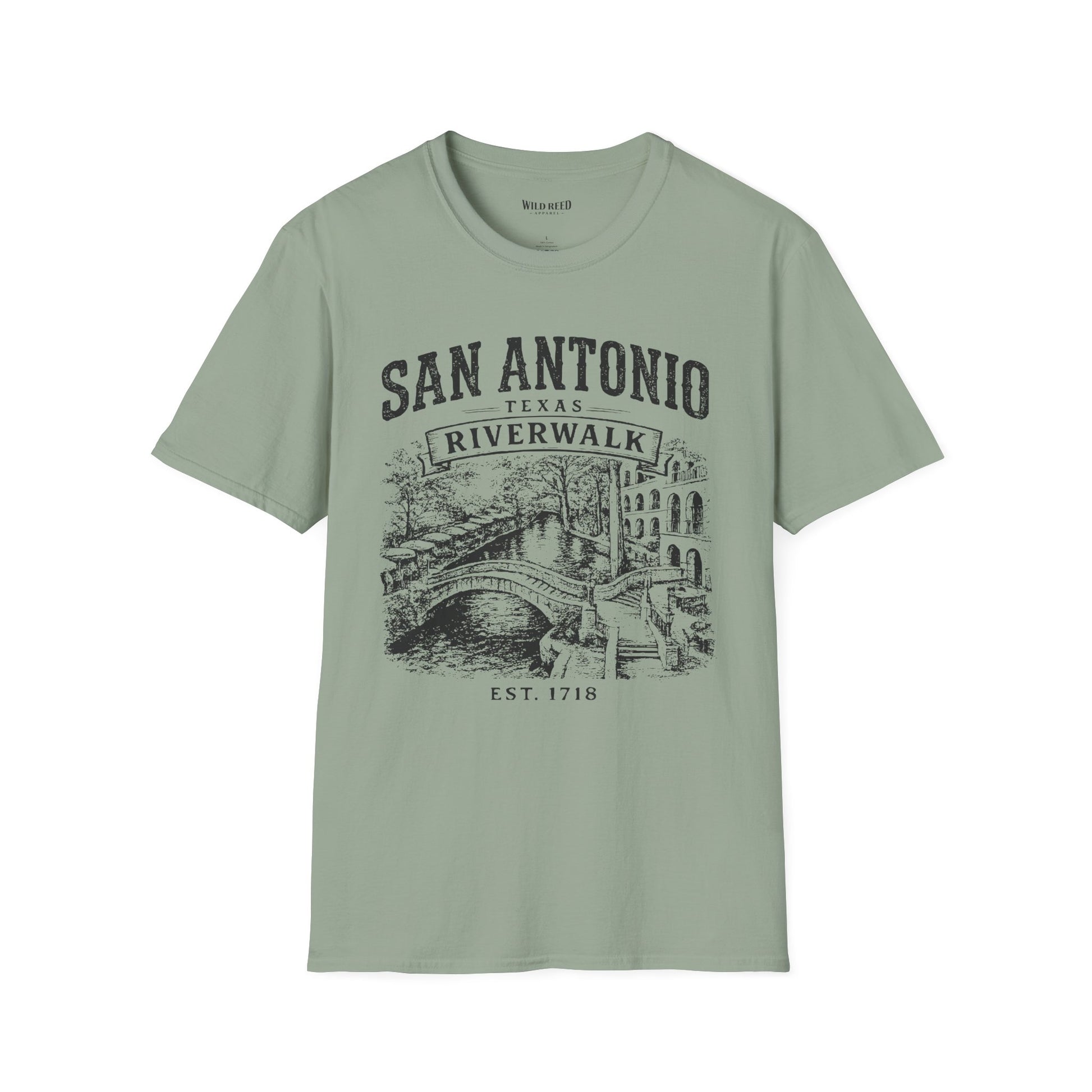 A sage short-sleeve t-shirt with a dark gray graphic print on the front reading 'SAN ANTONIO RIVERWALK TEXAS EST. 1718' above an illustration of a river scene with a bridge.