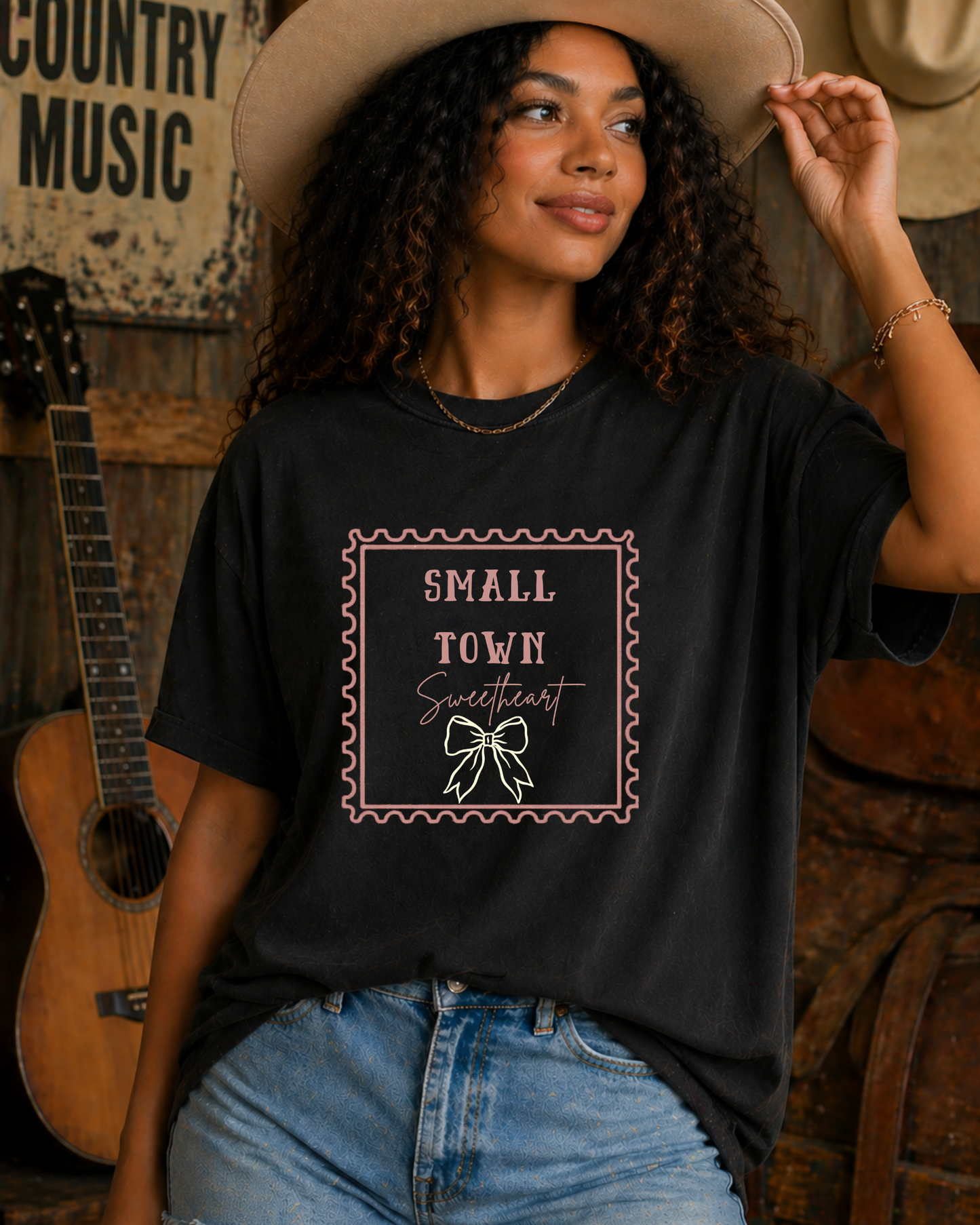 Woman wearing black Small Town Sweetheart western graphic tee holding cowboy hat