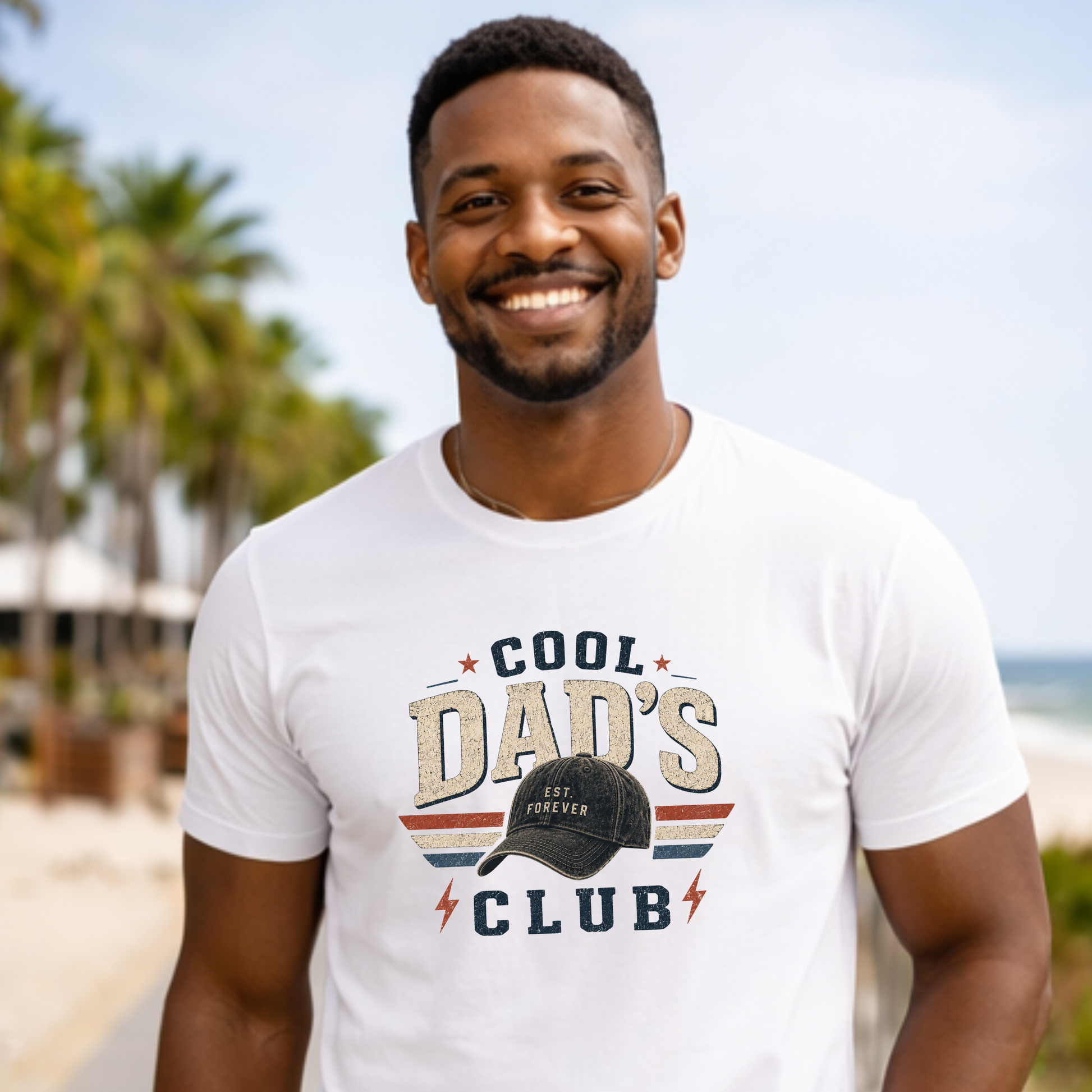 Man wearing a white t-shirt with 'Cool Dad's Club' text and graphic, standing outdoors with palm trees in the background.