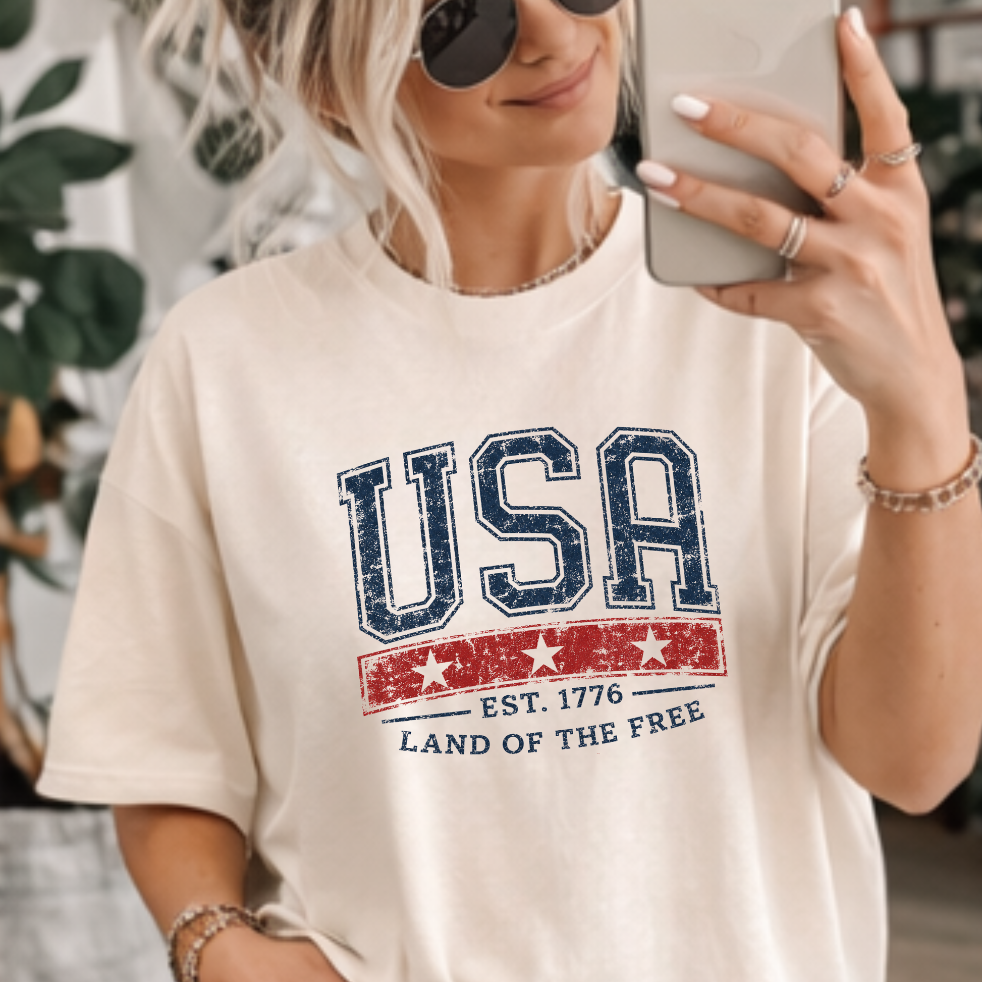 Vintage USA Est. 1776 patriotic graphic tee with distressed navy collegiate lettering and red Americana stripe on ivory shirt