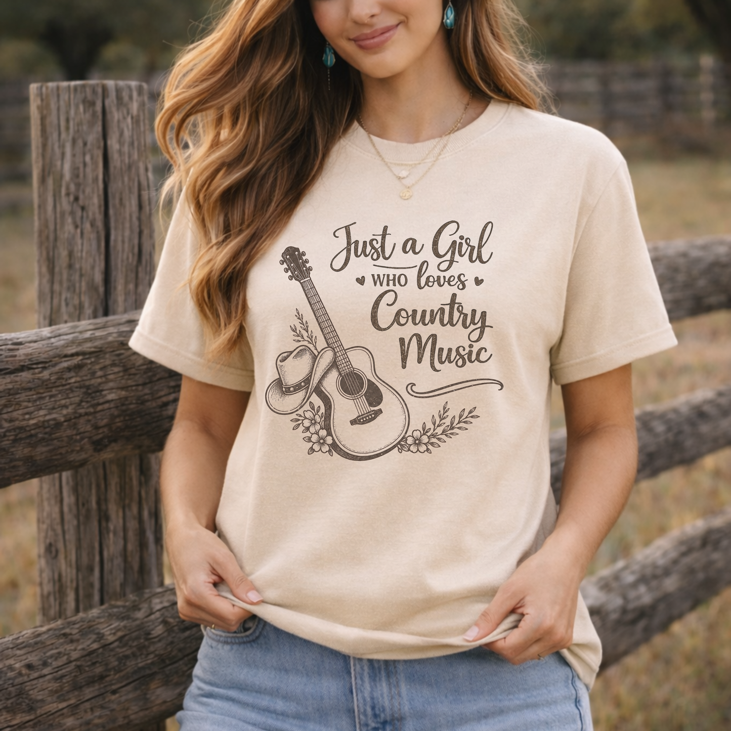 Woman wearing a cream western graphic tee with Just a Girl Who Loves Country Music guitar and cowboy hat design while outside next to a fence