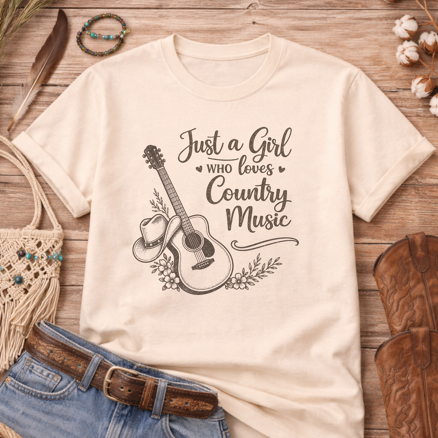 Beige t-shirt with guitar and cowboy hat graphic and text 'Just a Girl Who Loves Country Music' on a wooden surface with rustic items.