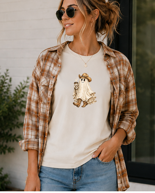 Woman smiling wearing a vintage cowgirl ghost graphic t-shirt featuring a smiling ghost wearing a cowboy hat and cowboy boots while holding a coffee cup with a cow print sleeve on a soft natural Gildan tee by Wild Reed Apparel.