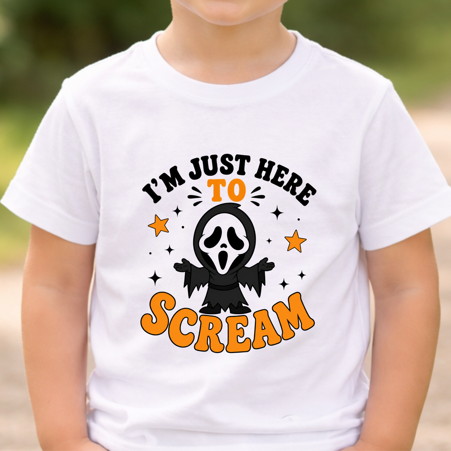 A child wearing a white short-sleeve T-shirt with a Halloween graphic that reads 'I'M JUST HERE TO SCREAM' in black and orange lettering, with a ghost face character and stars in the center.