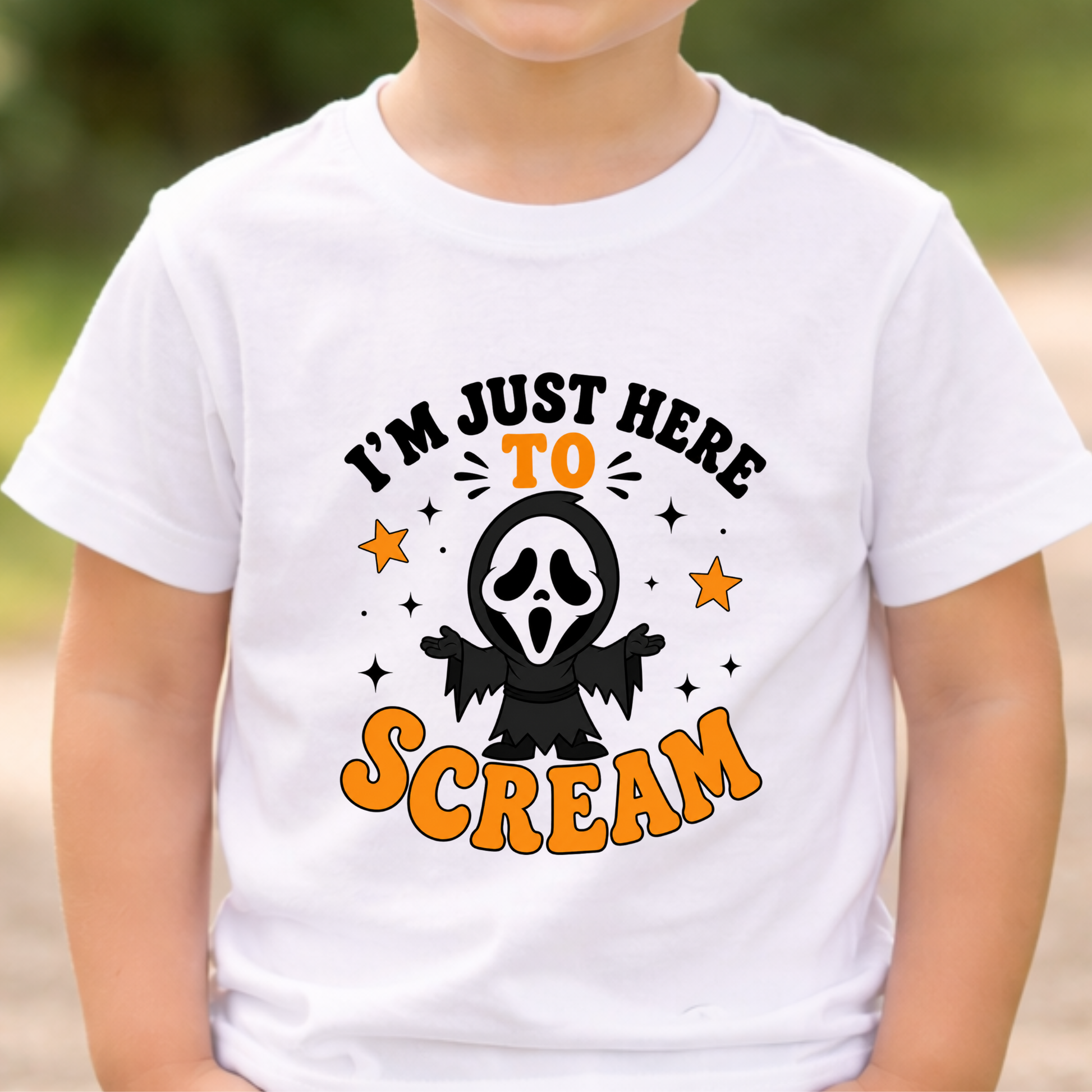 A child wearing a white short-sleeve T-shirt with a Halloween graphic that reads 'I'M JUST HERE TO SCREAM' in black and orange lettering, with a ghost face character and stars in the center.