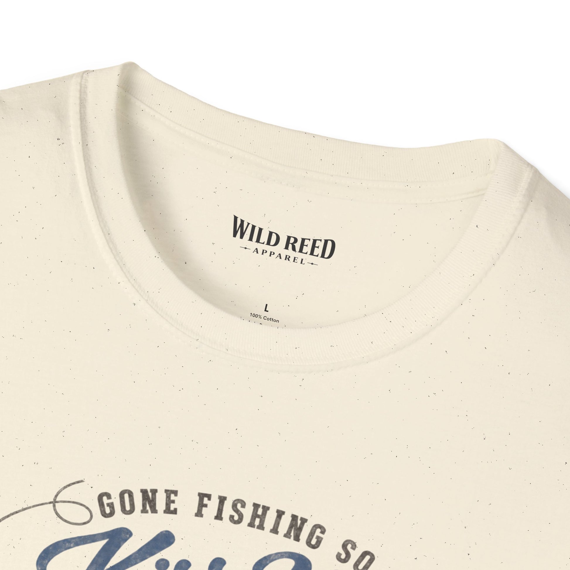 Close-up of a cream-colored t-shirt with a subtle speckled texture, showing the inner neck label 'WILD REED APPAREL' and the top of a graphic print that reads 'GONE FISHING SO'.