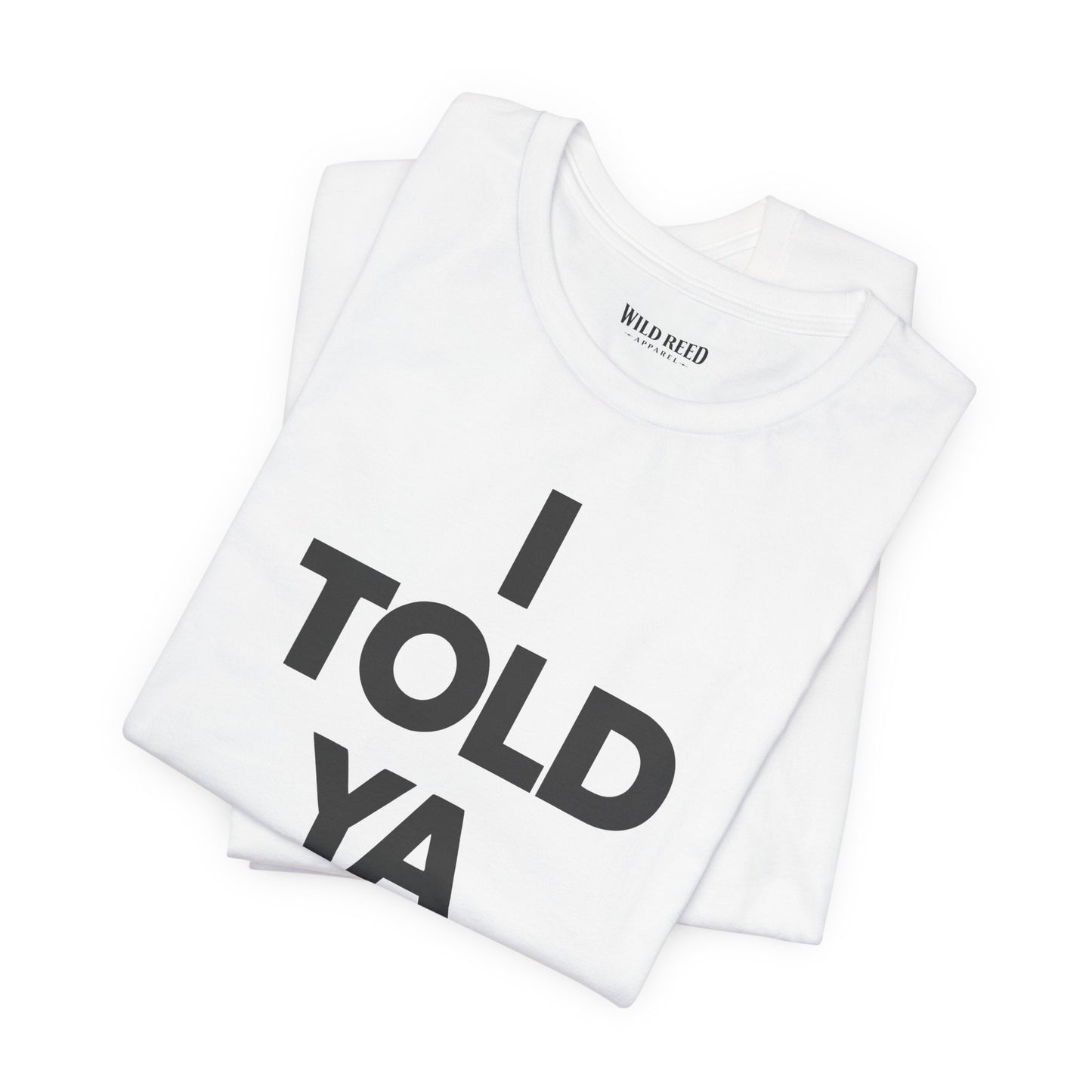 A folded white t-shirt with the text 'I TOLD YA' printed in bold black letters, displayed on a clean white background. The inner collar shows the brand name 'WILD Reed'.