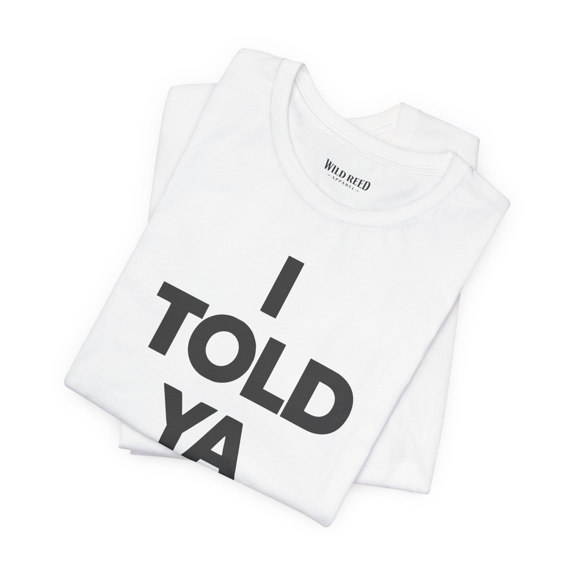 A folded white t-shirt with the text 'I TOLD YA' printed in bold black letters, displayed on a clean white background. The inner collar shows the brand name 'WILD Reed'.