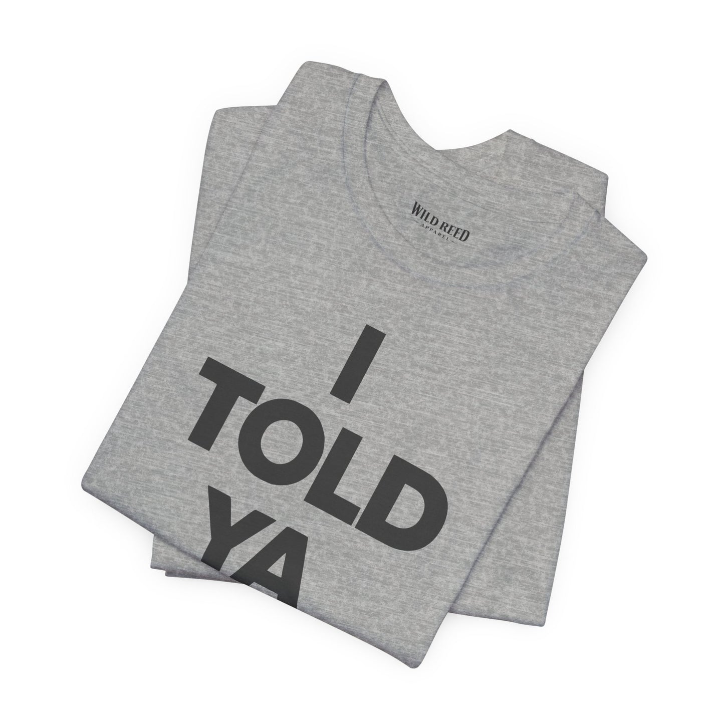 A folded heather gray t-shirt with bold black text reading 'I TOLD YA' on the front, displayed on a clean white background. The inner neck label shows the brand 'Wild Weed'.