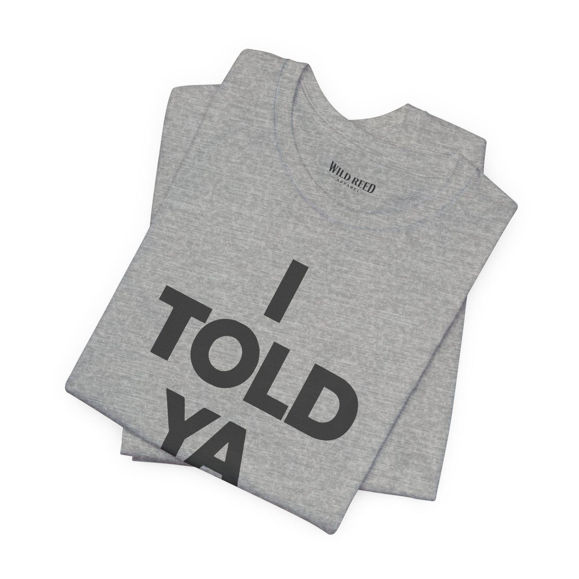 A folded heather gray t-shirt with bold black text reading 'I TOLD YA' on the front, displayed on a clean white background. The inner neck label shows the brand 'Wild Weed'.